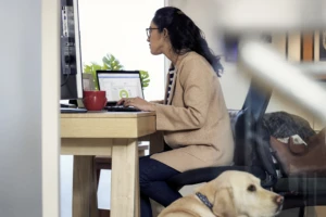Female working remotely from her home office on a Dell Latitude 13 device, with her dog by her side.