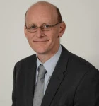 Photo of man in glasses with suit smiling at camera, Tim Clarke