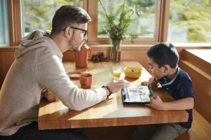 Father and son sit at breakfast table working on Acer Spin 1 2-in-1 tablet with touch screen using OneDrive.