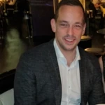 Blair Lochrie, a man with dark hair in a business suit posing for the camera and smiling.