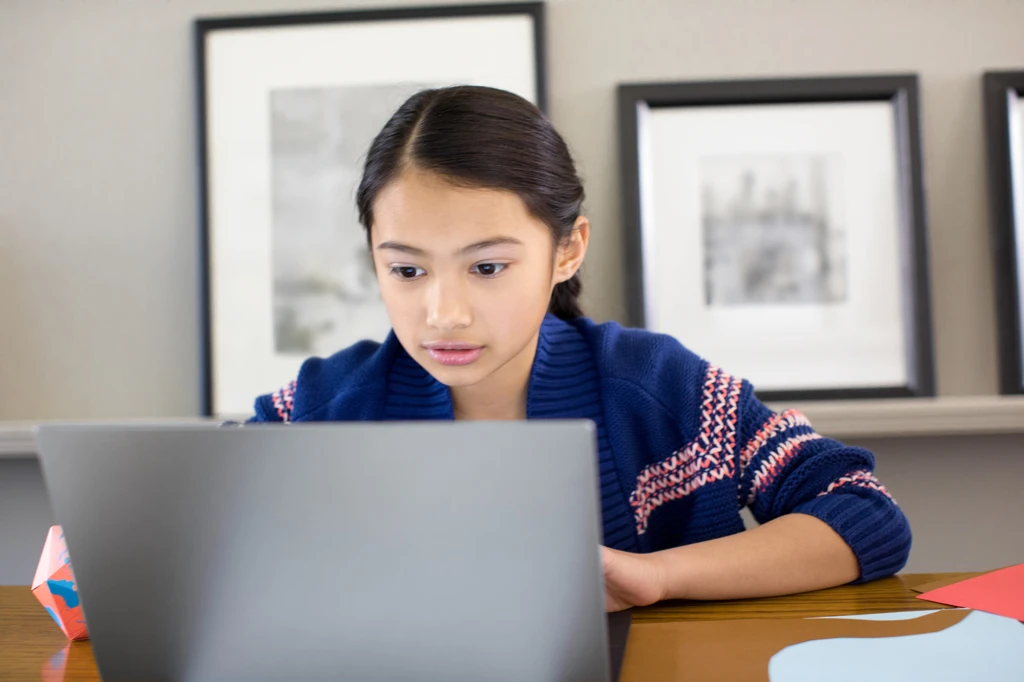 Female youth or child using laptop in family room.