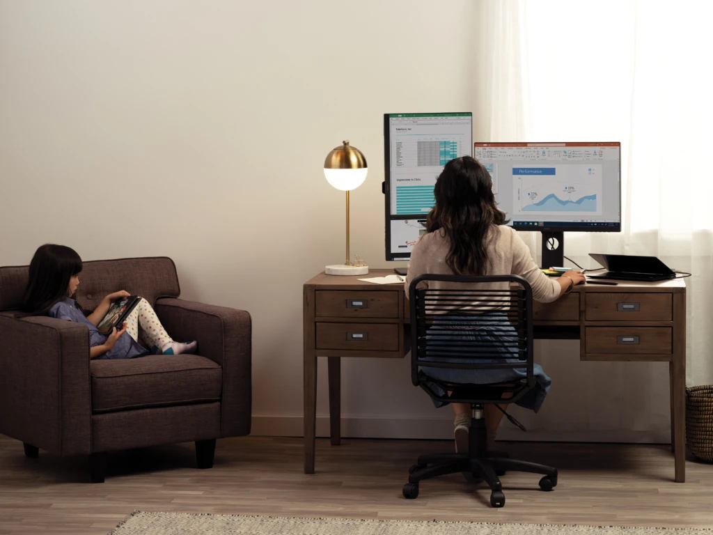 A woman working at a home desk while her child is remote learning next to her. In the new normal, we'll need to support flexible working practices