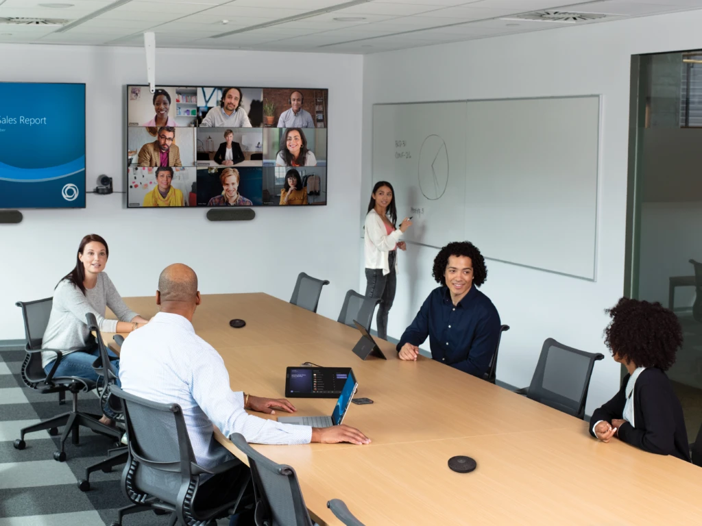 A group of people sitting in a meeting room with a Teams meeting screen showing remote participants.