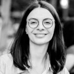 Ioana Marinescu, a woman with dark hair and glasses smiles at the camera