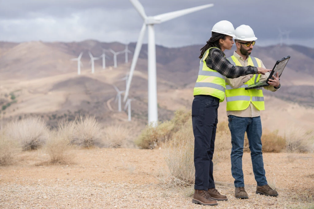 Two people standing in a wind energy farm, looking at data.