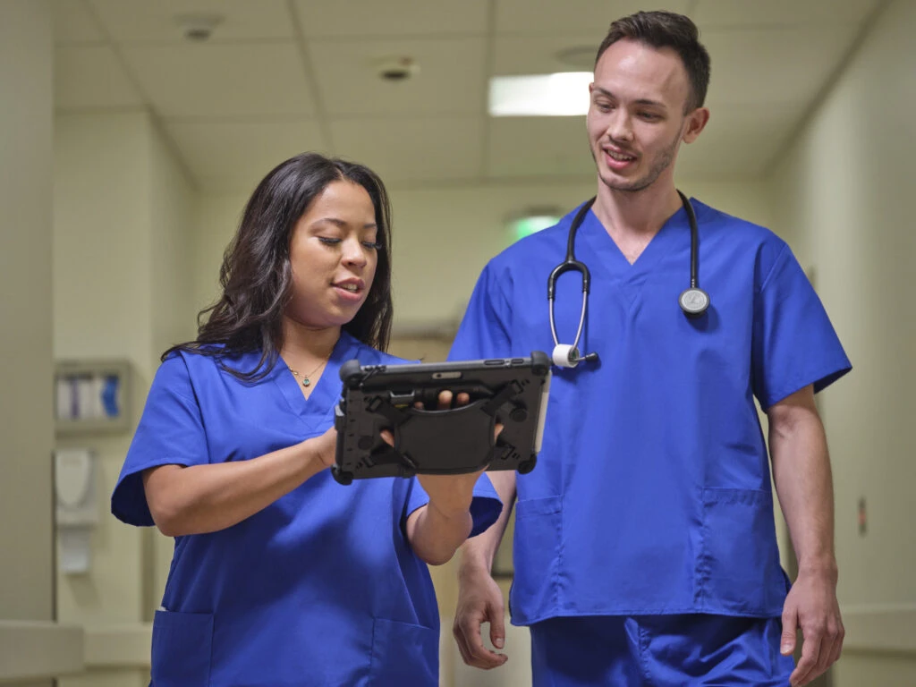 Two healthcare workers standing in the hall looking at the screen of a Surface Go 3.