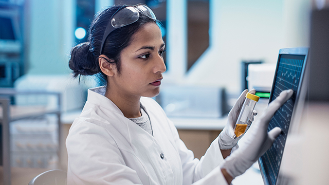 Woman in lab goggles and gloves working on a monitor.