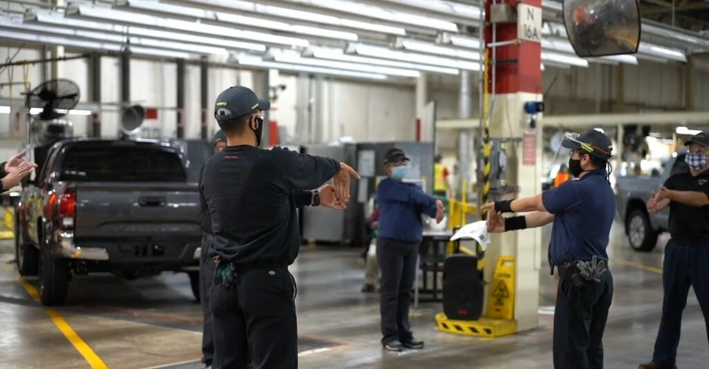 A group of Toyota employees do wrist mobility exercises and stretches together on the factory floor.
