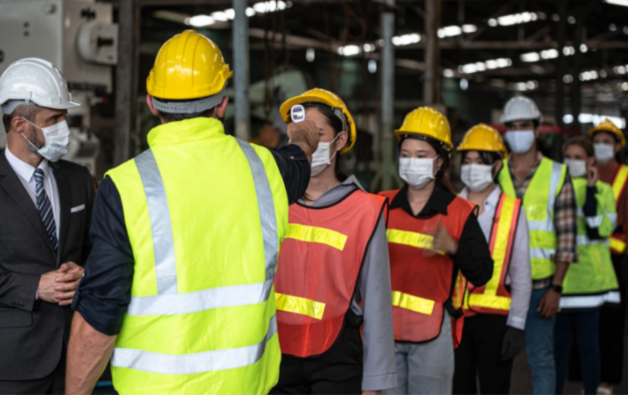 Fila de trabalhadores e um homem aferindo a temperatura