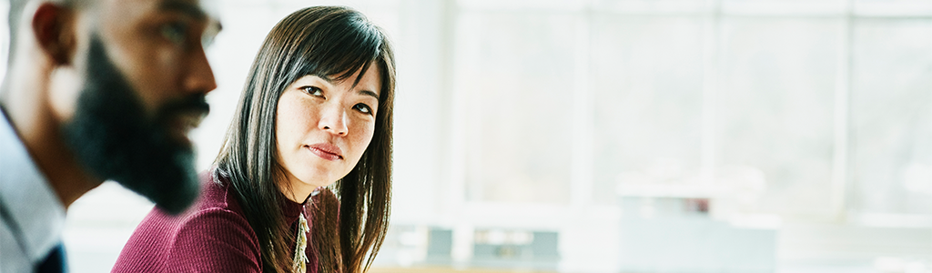 Uma mulher olhando um homem falando em uma sala de reunião