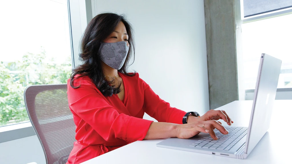 woman wearing a mask working on a Surface book