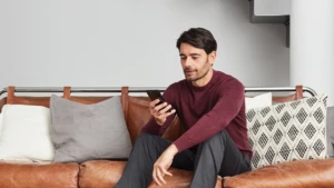 Man sitting on the couch looking down at the phone he is holding