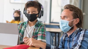 A child with a face mask and a man with a face mask and headphoneslooking at something on the Surface Pro