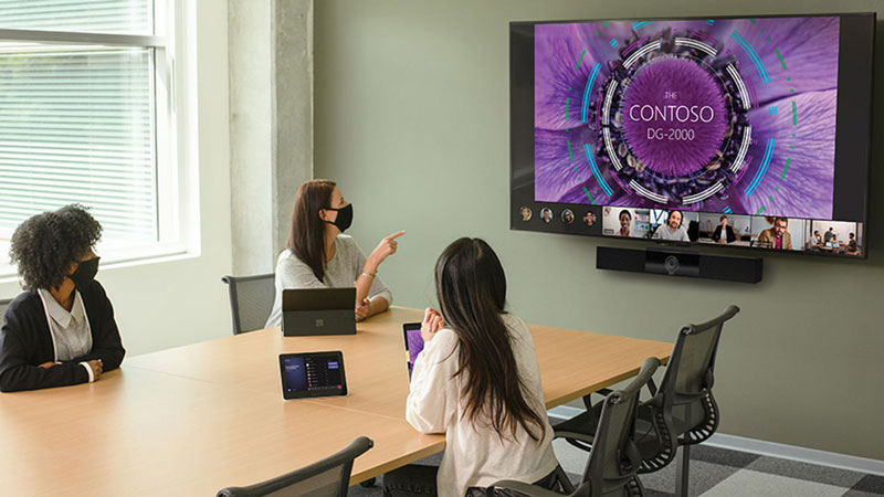 Team sitting around a board room table, engaged in a teams call on a large video wall.