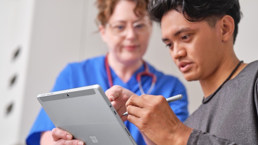 Man signing tablet with nurse pointing to a specific spot on the tablet
