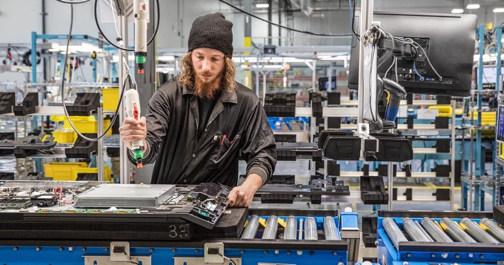 Male millennial factory worker building computer parts on an assembly line.