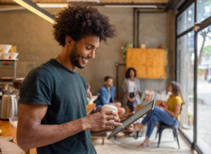 Happy man working online at a cafe while drinking a cup of coffee