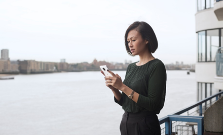 A woman stands on a ferry boat looking at her mobile device.