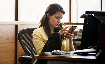 Image of a woman checking her phone while working at her desk.