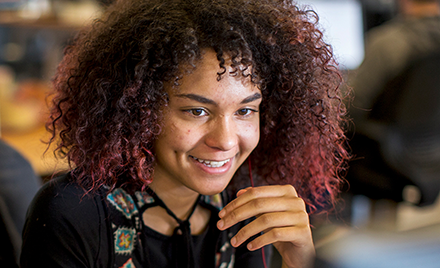 Image for: A woman sits at her work desk, smiling.