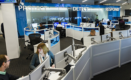 Image of a modern workplace. Above two workers speaking with one another are the words "Protect," "Detect," and "Respond."