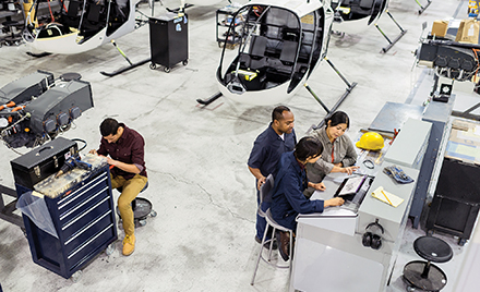 Image for: Image of workers assembling a helicopter. Several are gathered around a laptop.