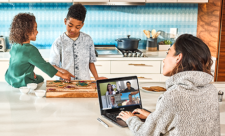 Image of a remote worker in a Microsoft Teams meeting while her children eat across from her on the kitchen countertop.