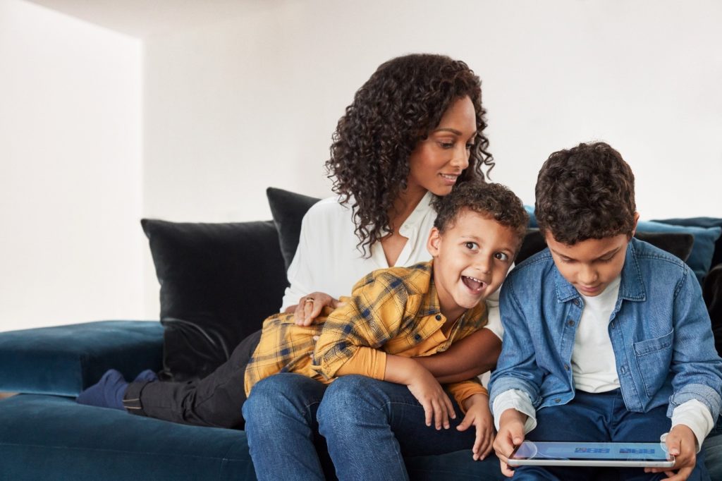 A family on a couch, one child holding a laptop.