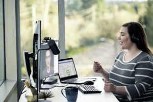 Female enterprise employee working remotely from her home office, chatting with a headset on.