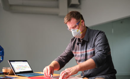 Image for: Manufacturing business owner wearing a mask and reviewing schedule in Shifts within Microsoft Teams.