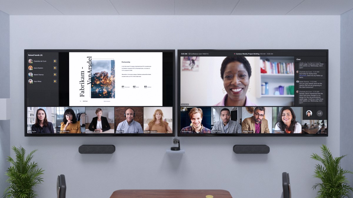 Remote attendees are across two front of room screens at eye level beside chat and a view of participants with raised hands.