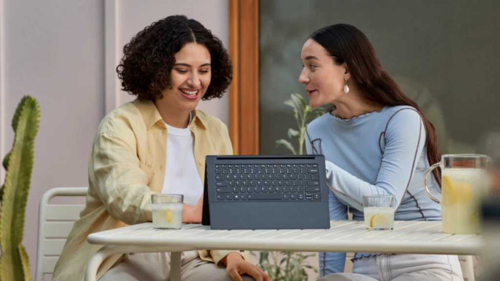 A photograph of two businesswomen talking while sitting at a table with a Microsoft Surface tablet outside a cafe. 