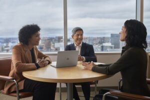 Three people meeting at a conference table with a Surface Laptop Go 2.