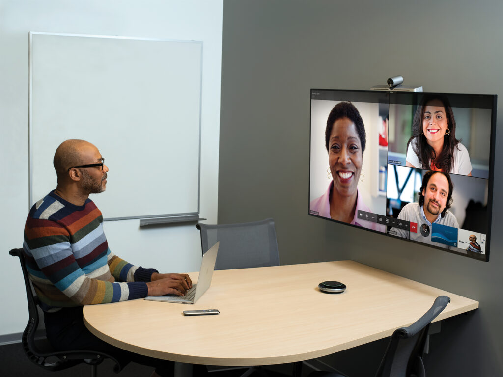 Man in a conference room, using Microsoft Teams for a meeting with three virtual participants