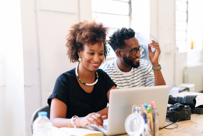 Two graphic designers sit in front of an open laptop.