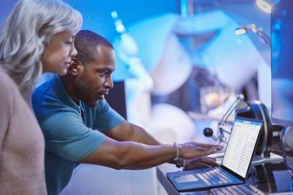 Azure solution in healthcare environment. Researcher engaged with Azure developer collaborating outside medical treatment room. Azure is powering the medical equipment is seen in the background. Azure provides the technology in the lab to deliver insights, analytics and healthcare advancements. Using technology to review medical research insights.