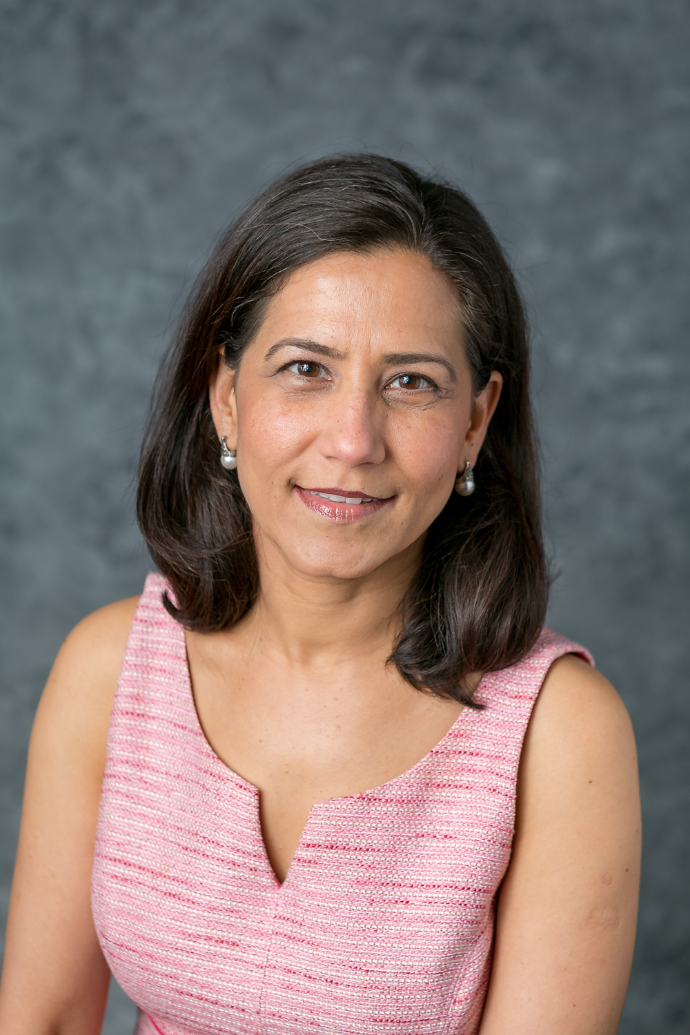 woman with dark hair wearing a pink shirt smiling at the camera