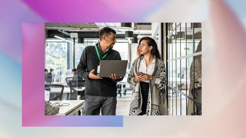 A man and a woman walking through an office hallway having a conversation.