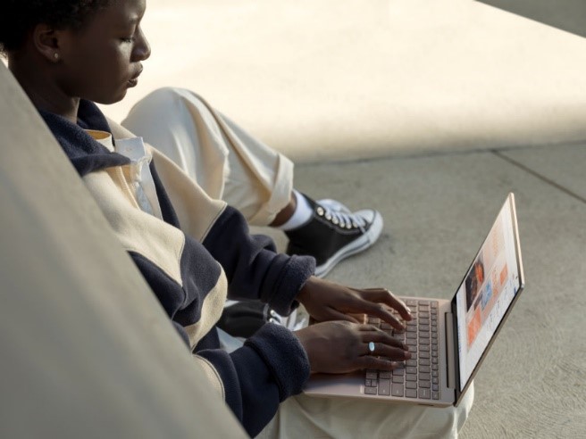 Decorative, a student sitting on the ground outside typing on a laptop. 