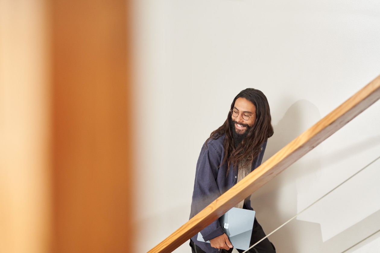A man ascending a stairway holding a Surface laptop