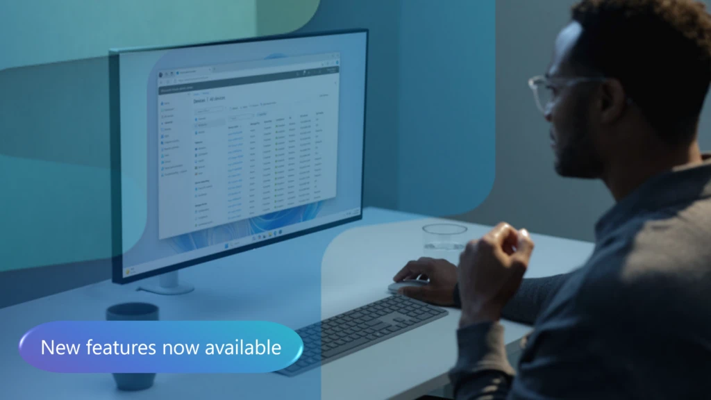 A man sitting at a desk looking at a computer screen; button overlay reads "New features now available"