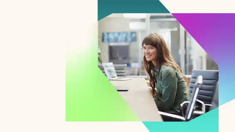 Smiling woman sits at a conference table with a laptop in a bright modern office, framed by overlapping geometric shapes in green, teal, purple, and blue on a light background