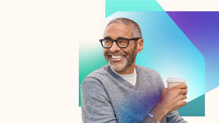 A man wearing glasses and a grey sweater holding a cup of coffee