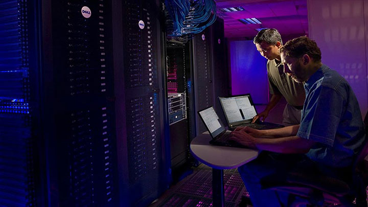 Two technicians working in a data center with purple lighting.