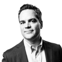 Toby Bowers wearing a suit and tie smiling at the camera