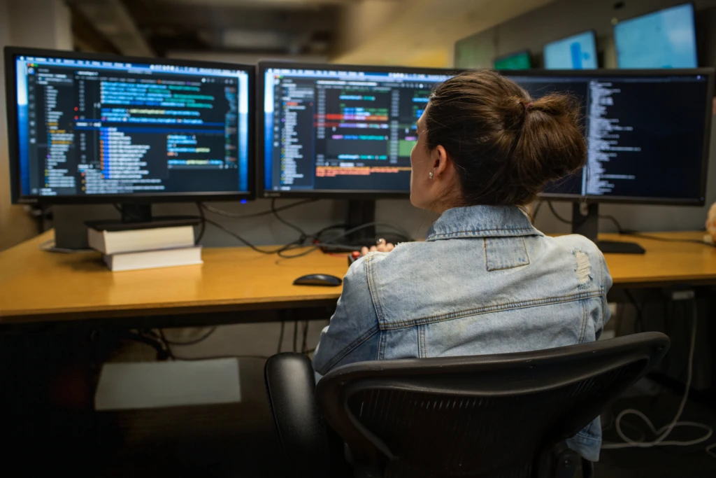 Female developer coding her workspace in an enterprise office, using Visual Studio on a multi-monitor set up.