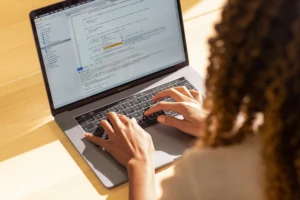 Real people, real offices. Black female developer coding on a MacBook Pro in the office, using Visual Studio. Hands on keyboard. Women who code, women developers, women engineers, code, develop, Black developer, engineer, Visual Studio, Azure.