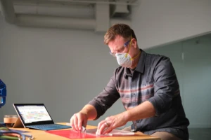 Manufacturing business owner wearing a mask and reviewing schedule in Shifts within Microsoft Teams. Male, mask, manufacturing, bags, Surface