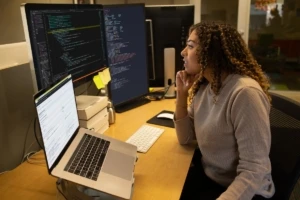 Female developer coding at her desk. She has customized her workspace with a multi-monitor set up and using Visual Studio for Mac.