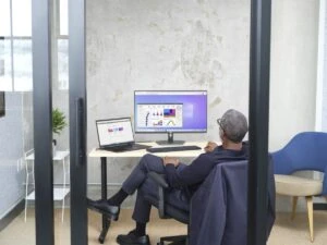 Man sitting in an office viewing Power BI UI within Windows 365. Shown on Windows 10 Keywords: sitting at a desk; crossed legs; Markus Long; Fabrikam; Enterprise; mousing; laptop; desktop; one screen; one monitor; dual screens; Edge browser; backside of person; Swanson